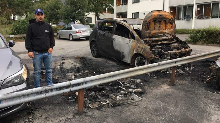 Hasan Tümtürk stands in front of his and other cars damaged by fire at a parking lot.